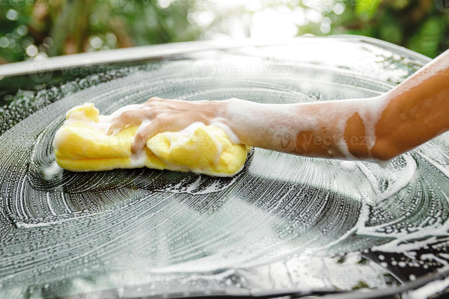 Female hand with yellow sponge washing car's windshield photo