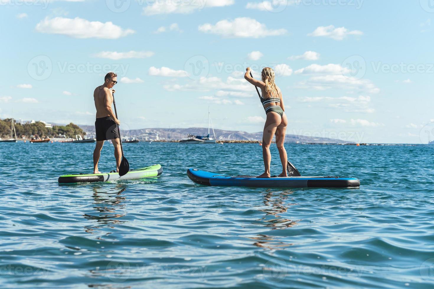 Male and female surfers riding standup paddleboards in ocean. photo