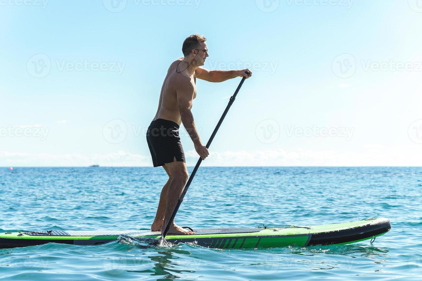 Young male surfer riding standup paddleboard in ocean. photo