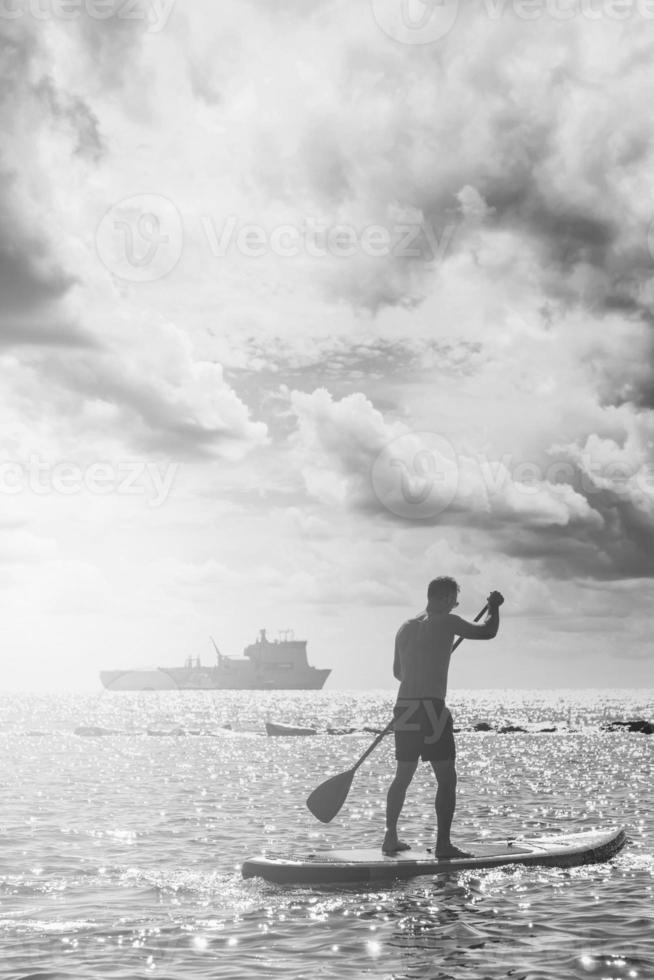 Young male surfer riding standup paddleboard in ocean. photo