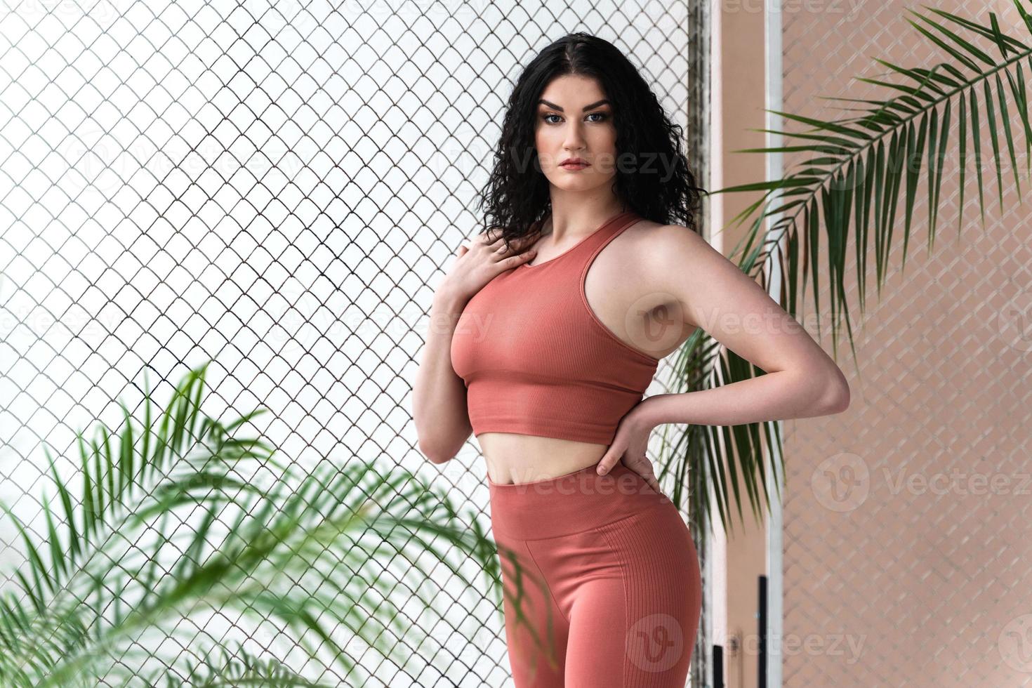 Young sportive woman with black wavy hair wearing  coral color sportswear photo