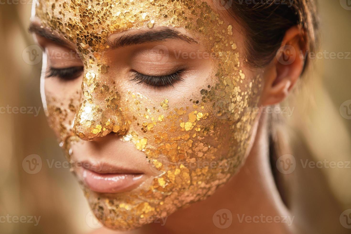 hermosa mujer con máscara dorada brillante en la cara para el tratamiento de la piel foto