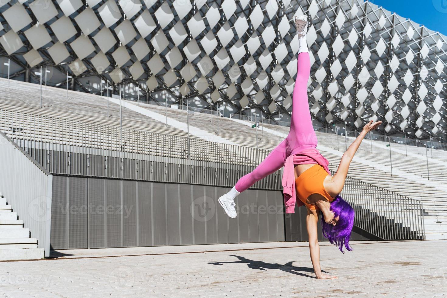 Carefree woman wearing colorful sportswear making cartwheel movement on the street photo