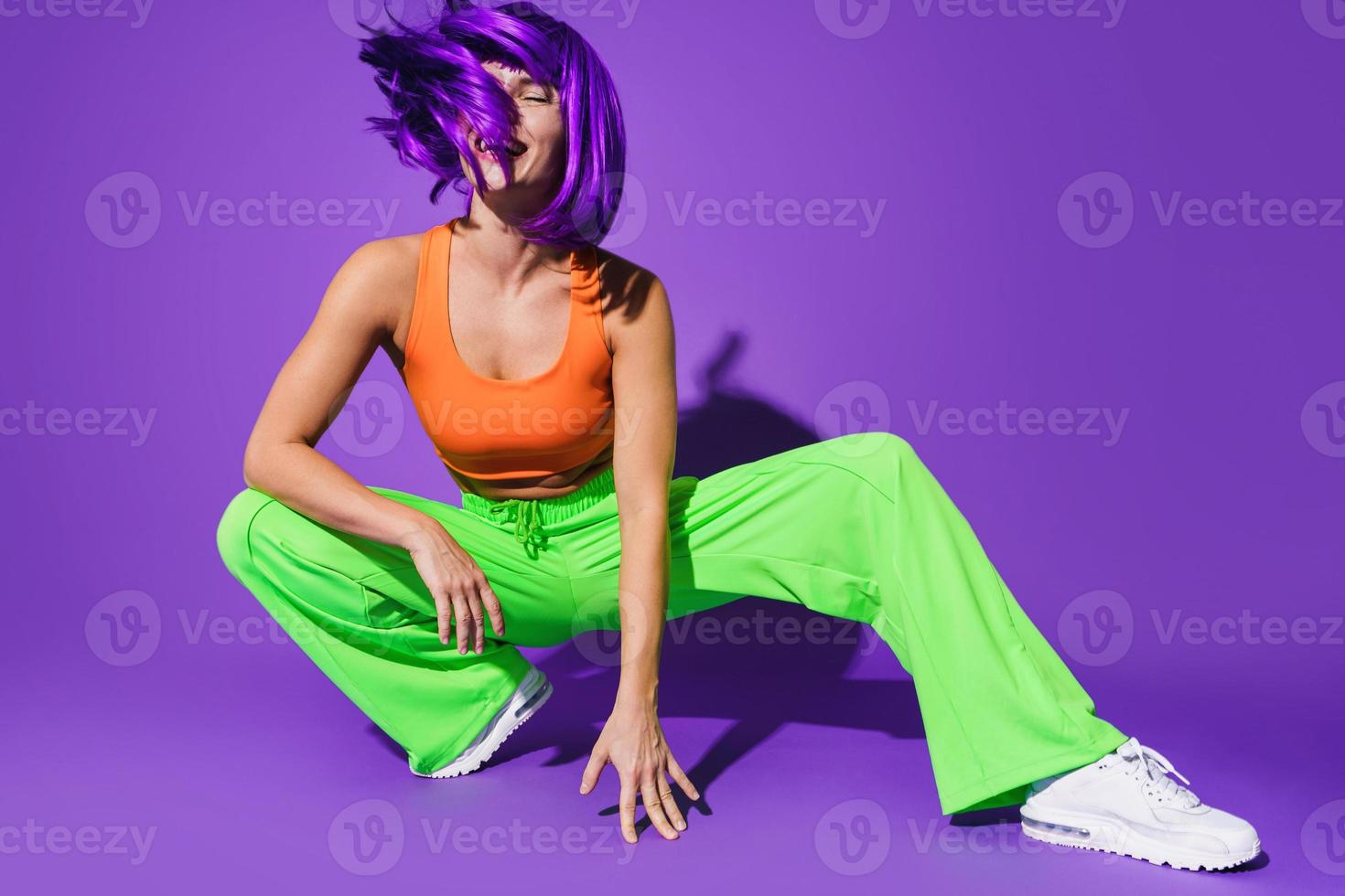 Carefree woman dancer wearing colorful sportswear having fun against purple background photo