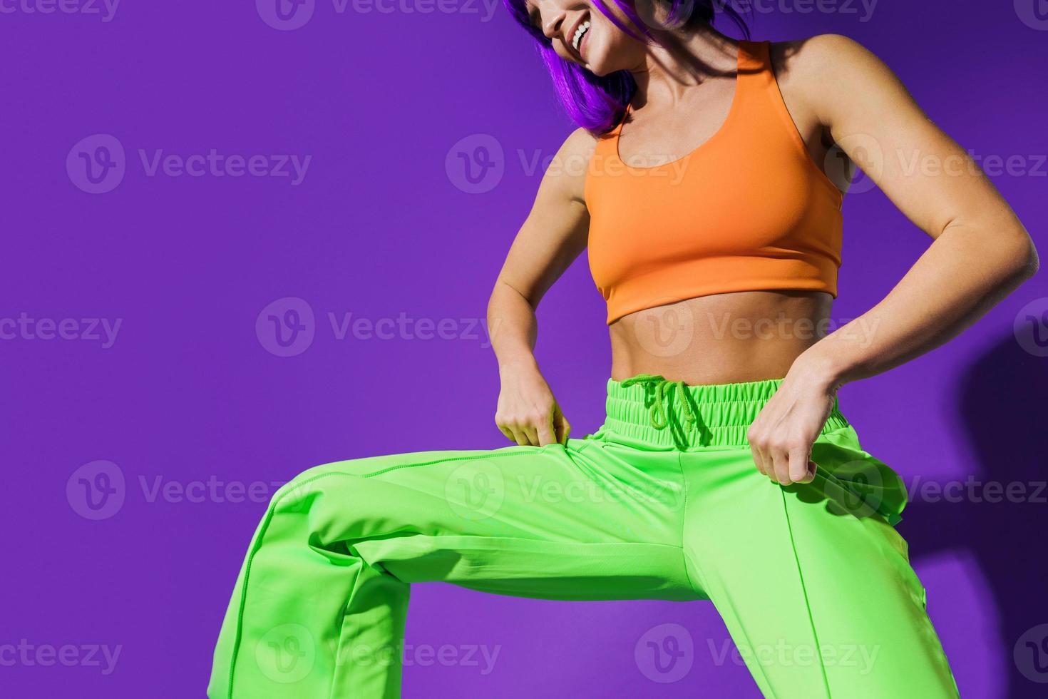 bailarina despreocupada que usa ropa deportiva colorida divirtiéndose contra el fondo púrpura foto