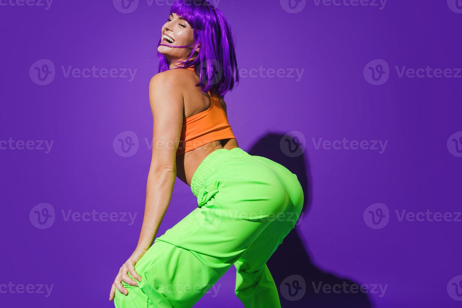 mujer despreocupada con ropa deportiva colorida twerking contra fondo púrpura foto