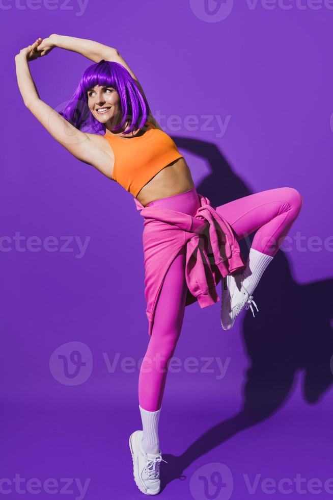 Bailarina despreocupada con ropa deportiva colorida actuando contra un fondo morado foto