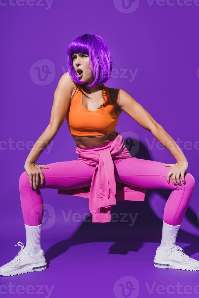 Carefree woman dancer wearing colorful sportswear performing against purple background photo