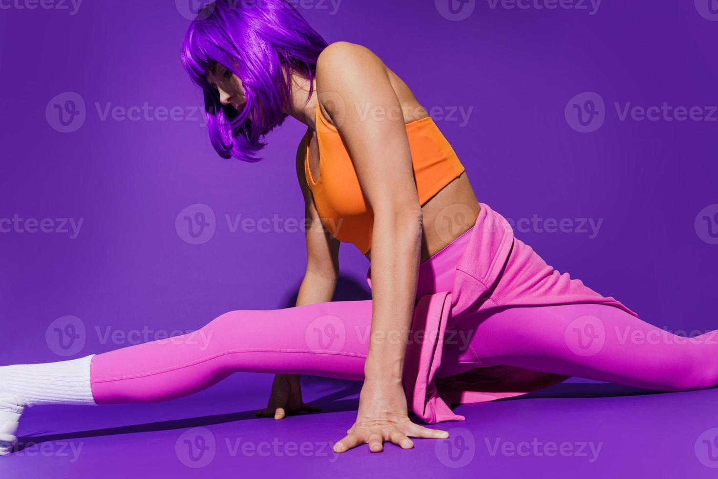 Woman wearing colorful sportswear doing splits against purple background photo