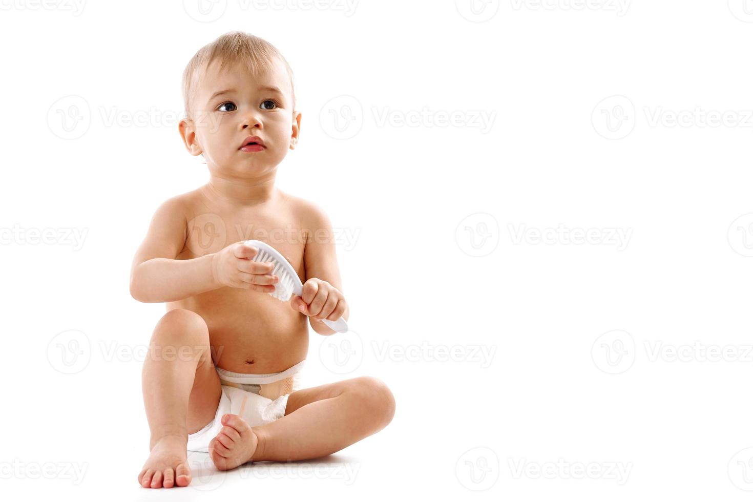 niño pequeño en pañales sentado y jugando con cepillo. foto