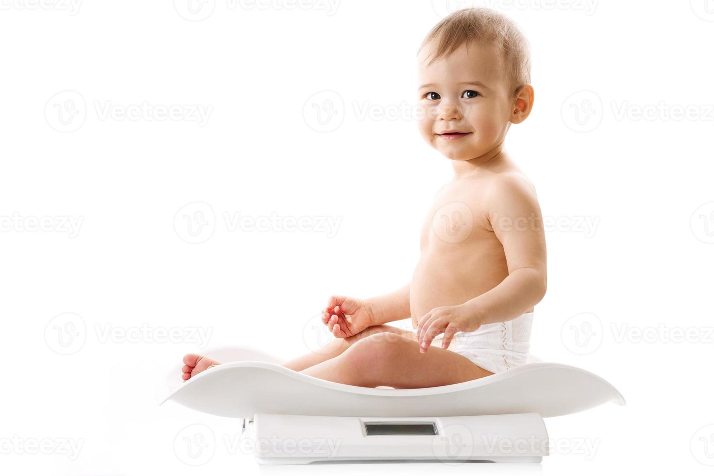 Weighing of a little boy in diaper sitting on scales. photo