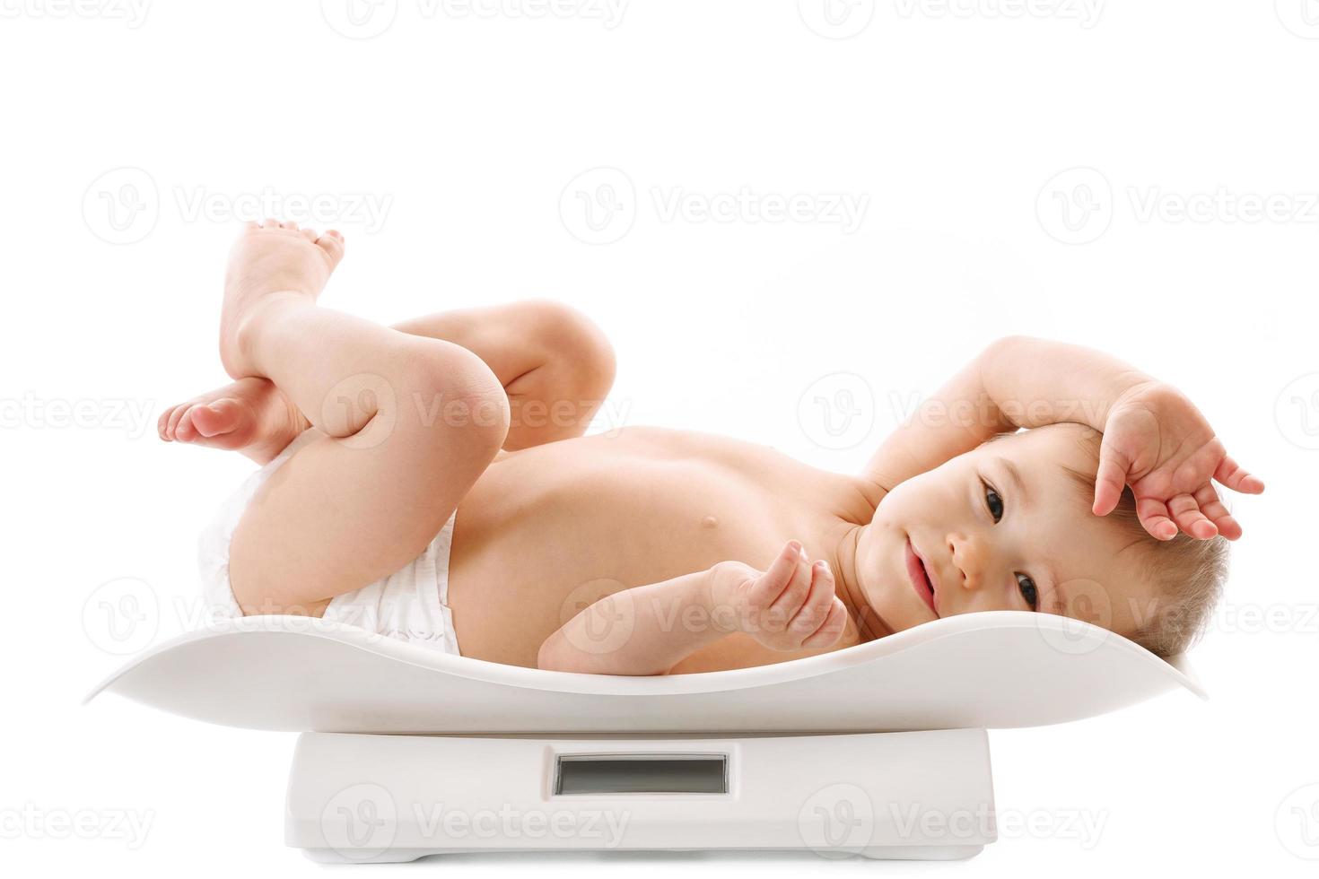 Weighing of a little boy in diaper lying on scales. photo