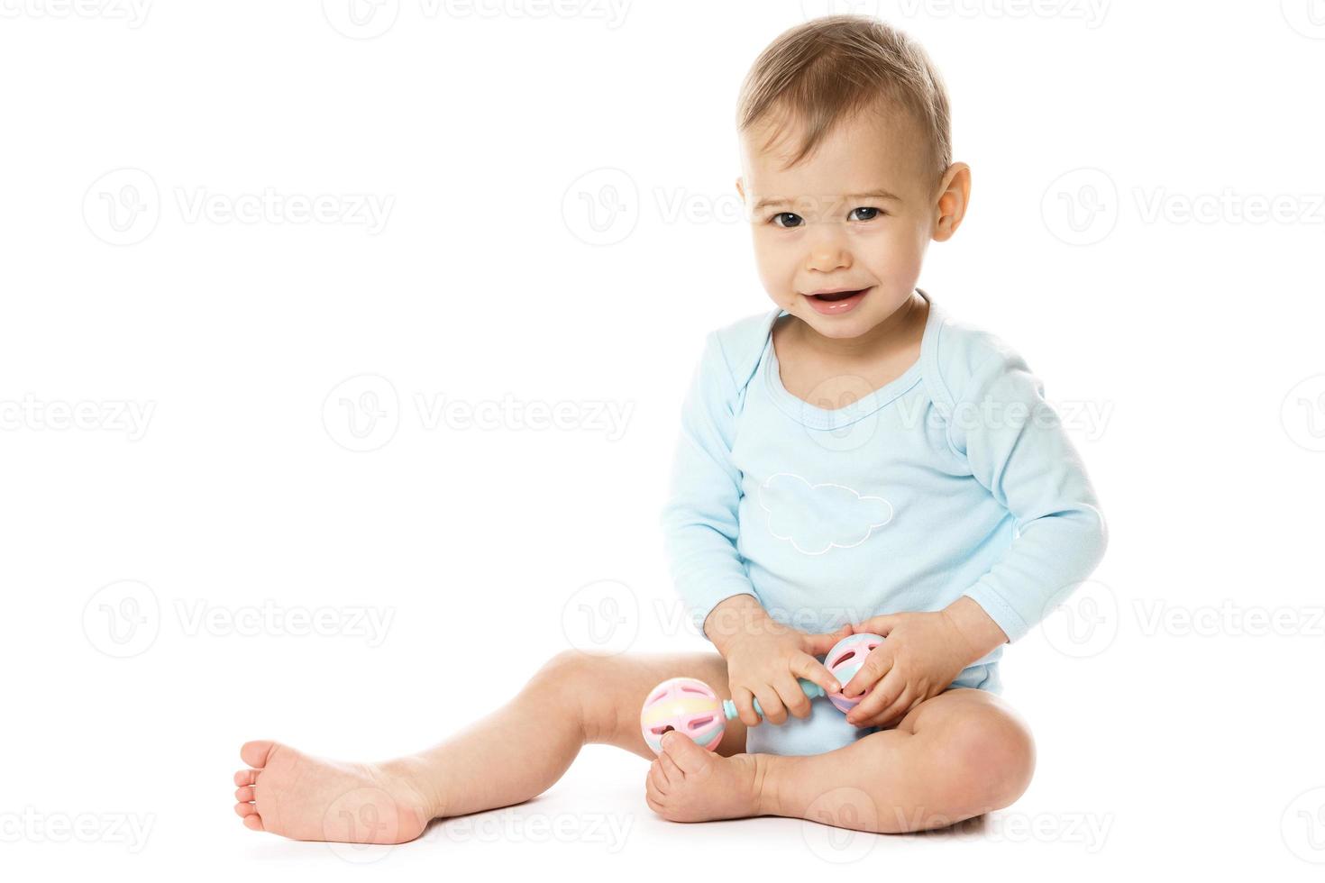 niño pequeño en mameluco sentado y jugando con sonajero de plástico. foto