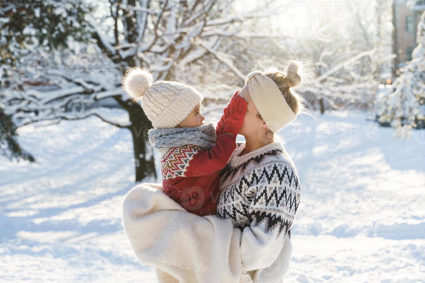 Young mother and her cute little son  playing peekaboo during sunny winter day photo