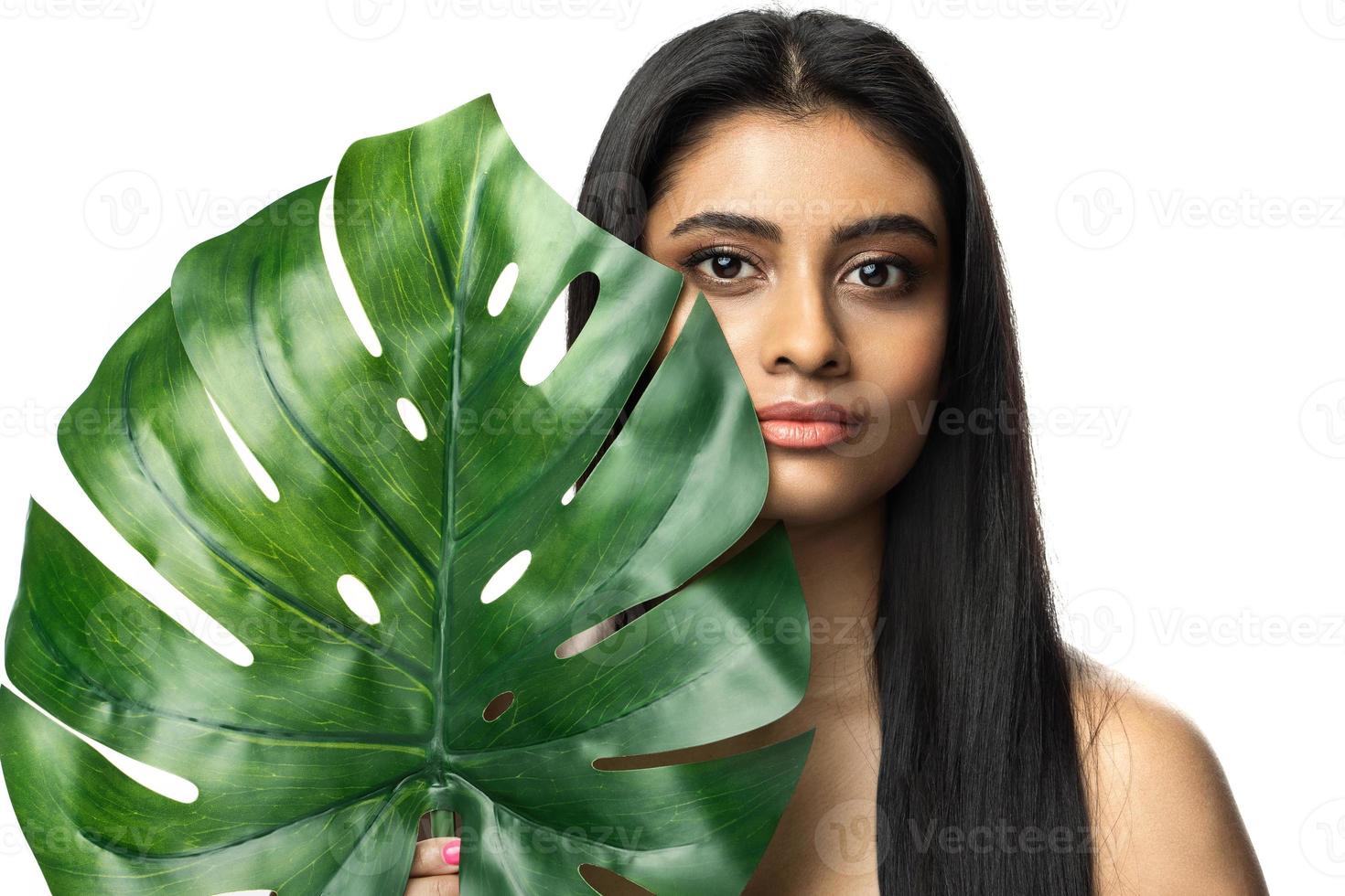 hermosa mujer india con una piel suave sosteniendo una hoja tropical verde foto