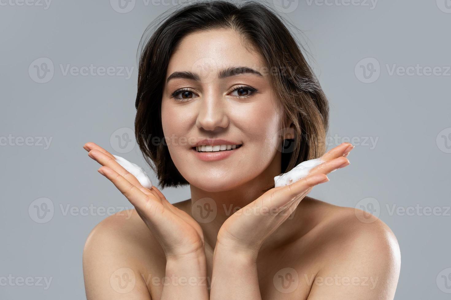 Beautiful brunette woman with a smooth skin applying cleansing foam on her face photo