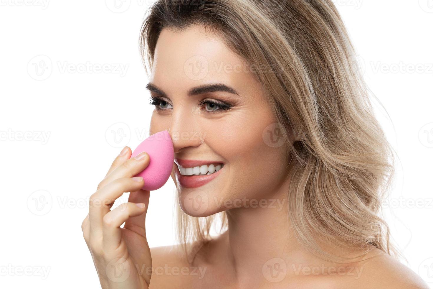 hermosa mujer con una piel suave sosteniendo una esponja de maquillaje sobre fondo blanco foto