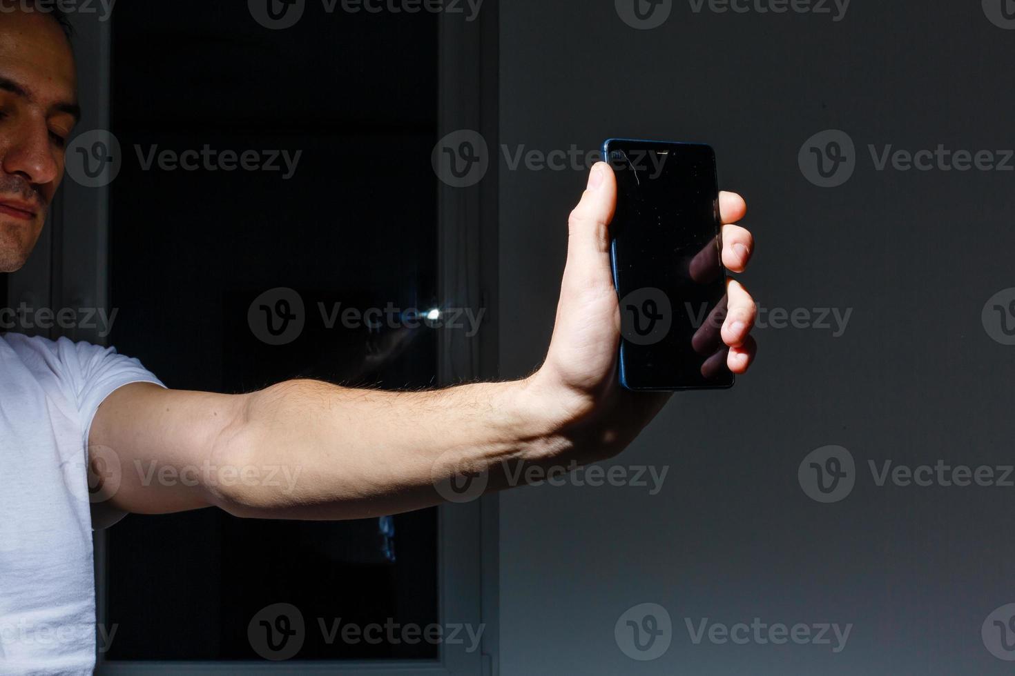 A young man is sitting holding a broken smart phone photo