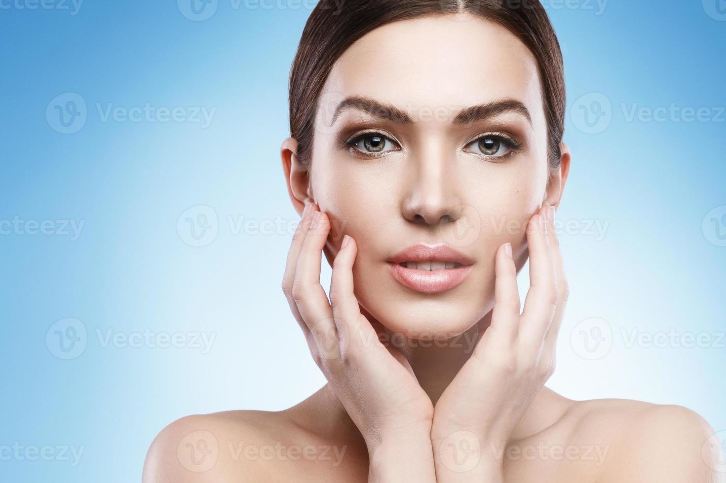 mujer joven con maquillaje natural y piel suave sobre fondo azul claro foto