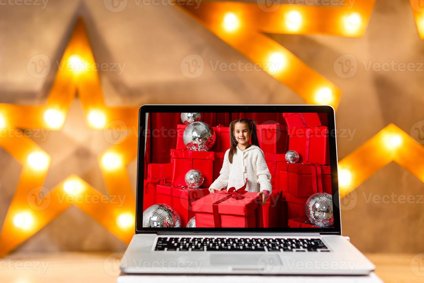 Image of open laptop with white screen on wooden table in front of christmas tree background. For mockup photo