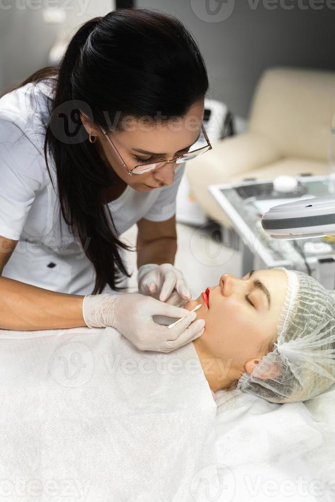 Permanent makeup artist and her client during lip blushing procedure photo