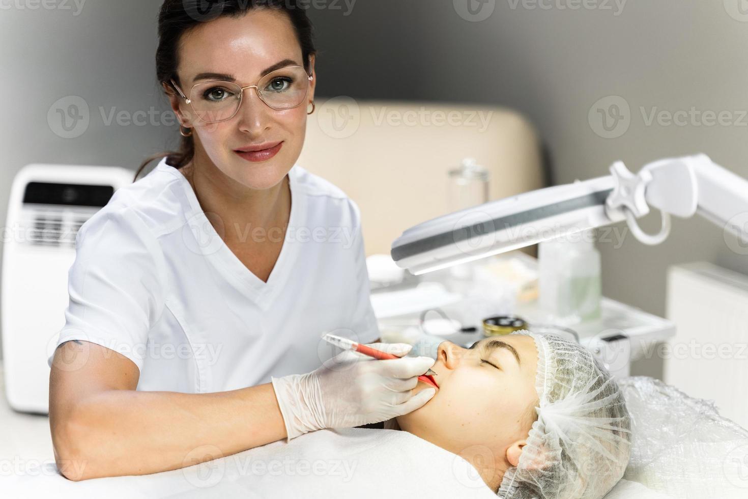 Permanent makeup artist and her client during lip blushing procedure photo