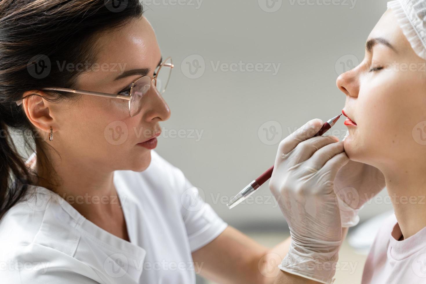 Permanent makeup artist and her client during lip blushing procedure photo