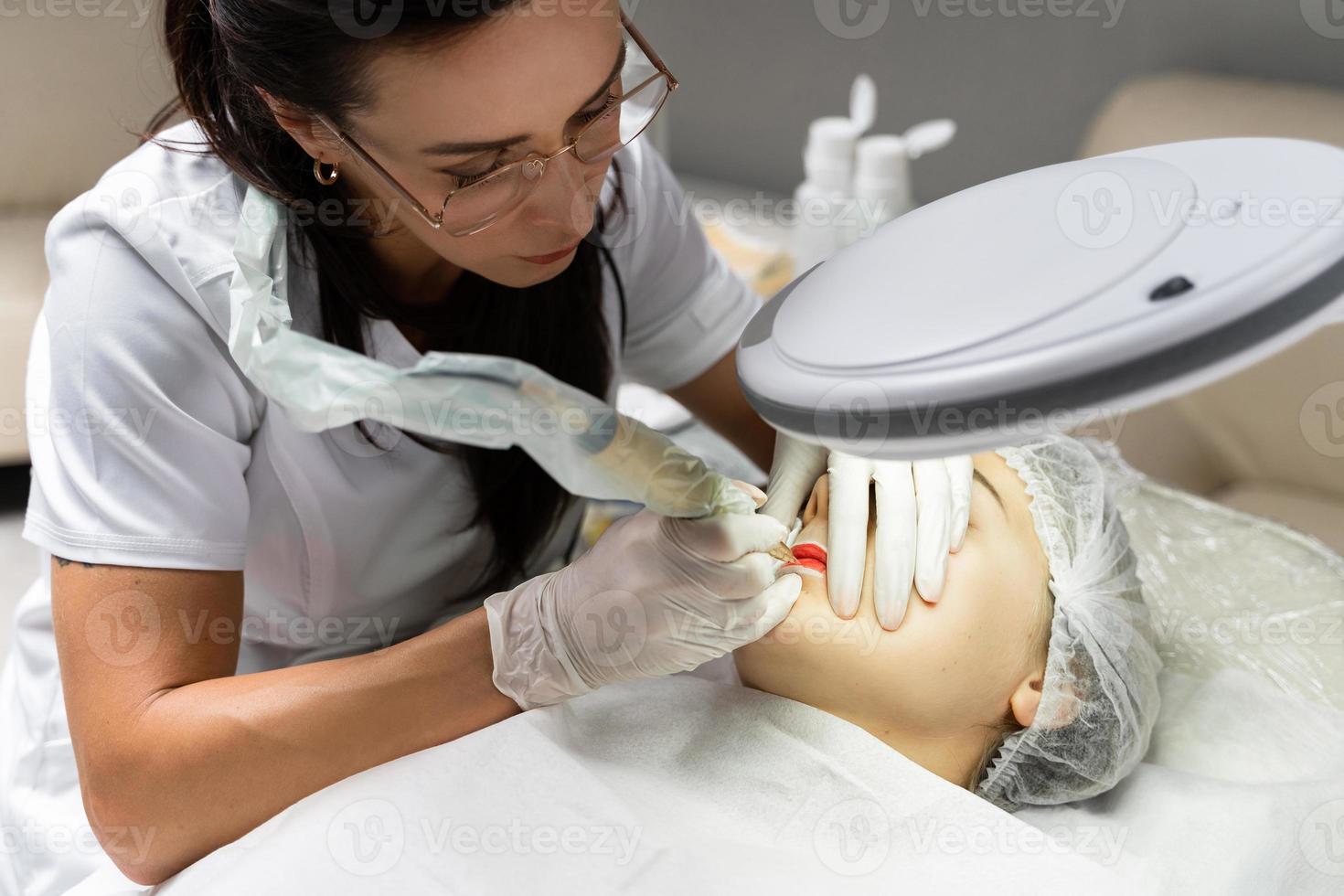 Permanent makeup artist and her client during lip blushing procedure photo