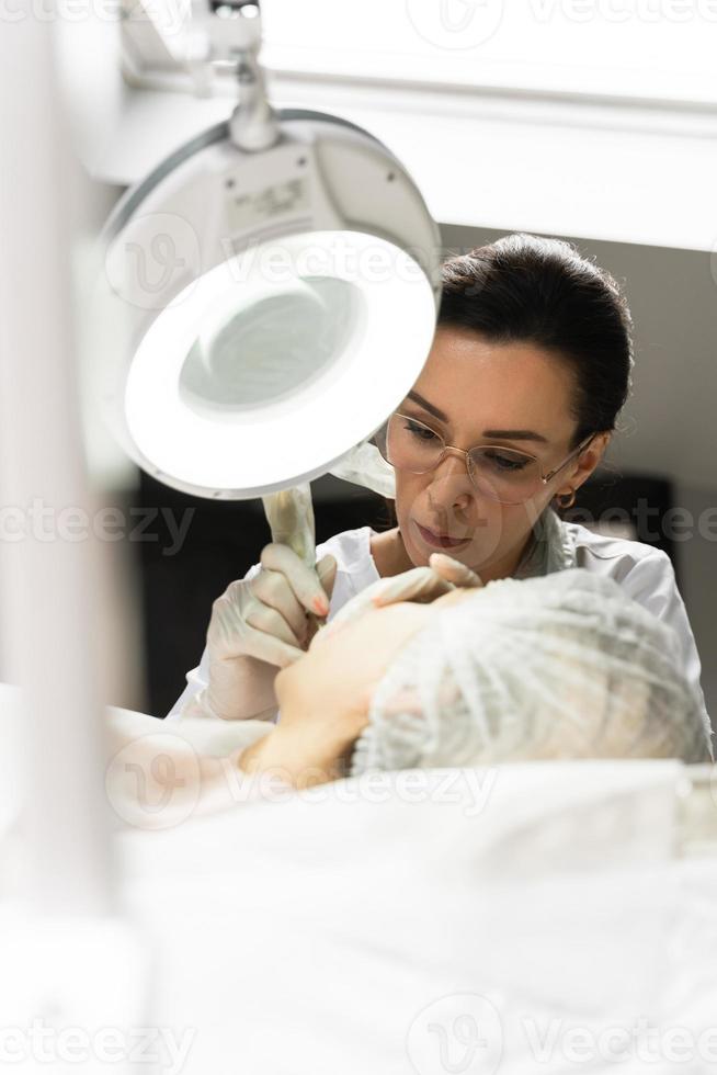 Permanent makeup artist and her client during lip blushing procedure photo