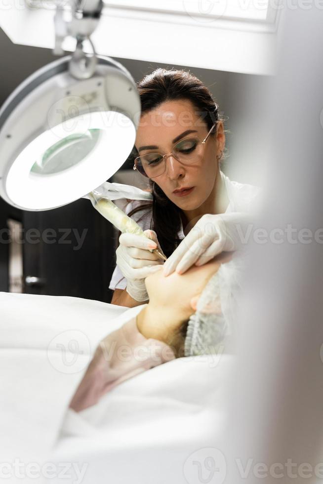 Permanent makeup artist and her client during lip blushing procedure photo