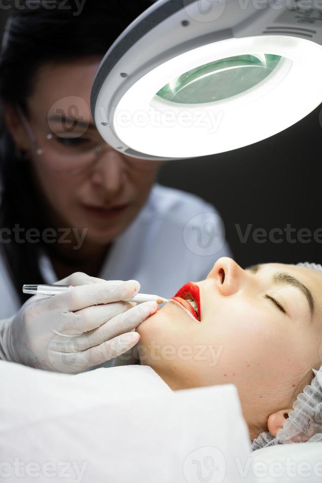 Permanent makeup artist and her client during lip blushing procedure photo