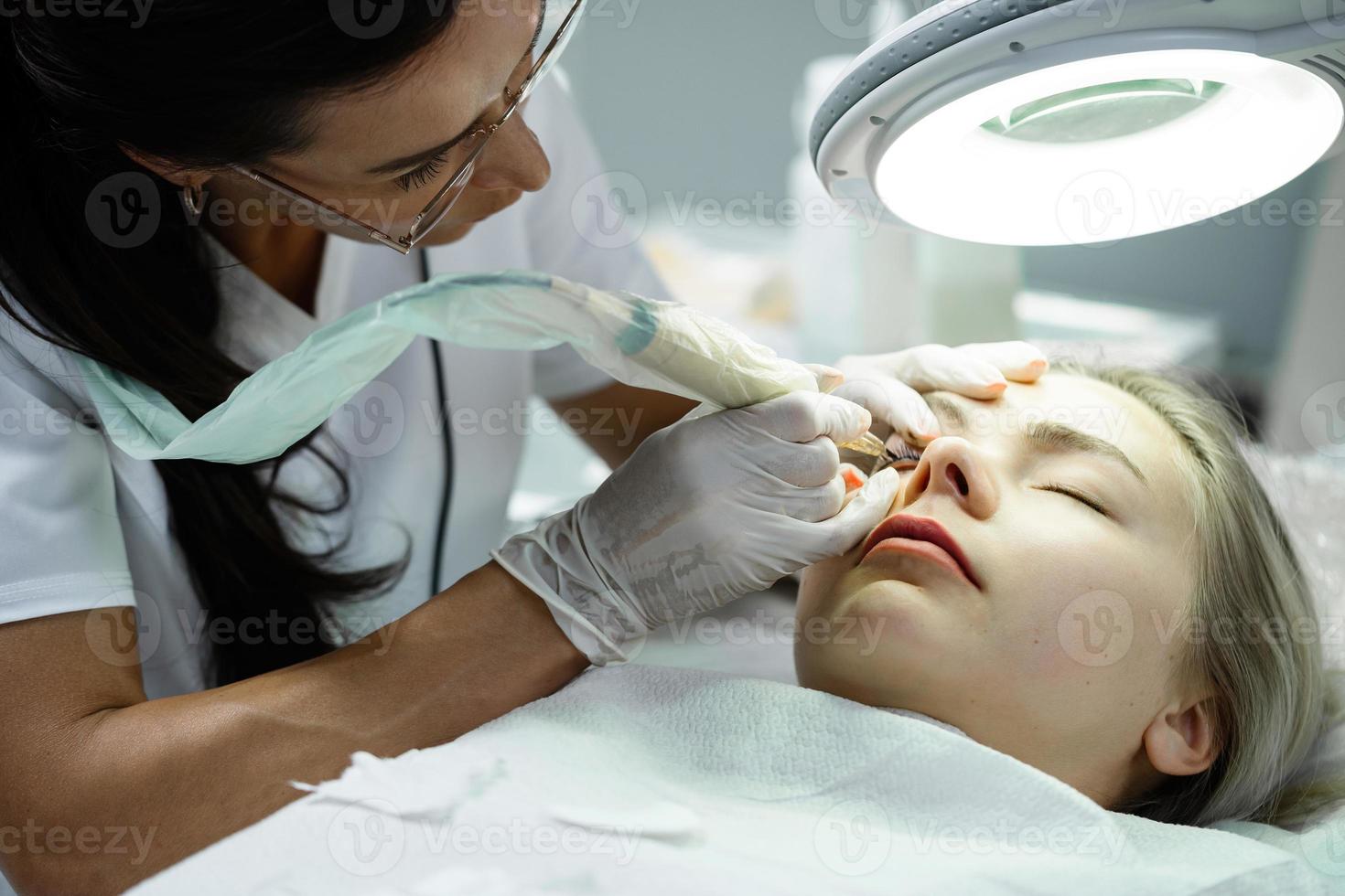 Permanent makeup artist and her client during lash line enhancement treatment photo