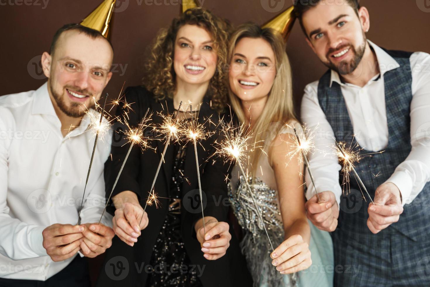 gente feliz con sombreros de fiesta sosteniendo chispas ardientes durante la celebración de vacaciones o eventos foto