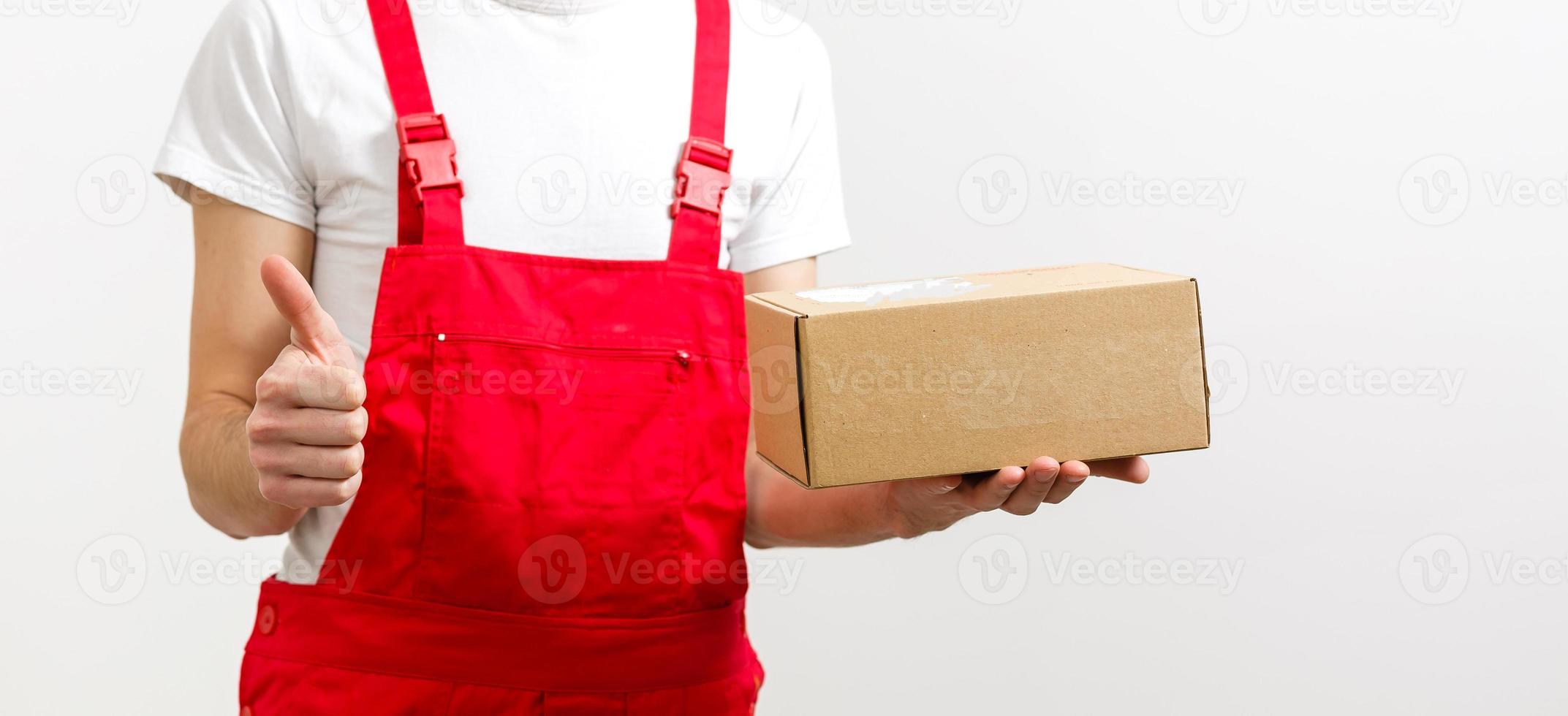 Mago de un joven y feliz repartidor con gorra roja de pie con un buzón de paquetes aislado sobre fondo blanco. foto