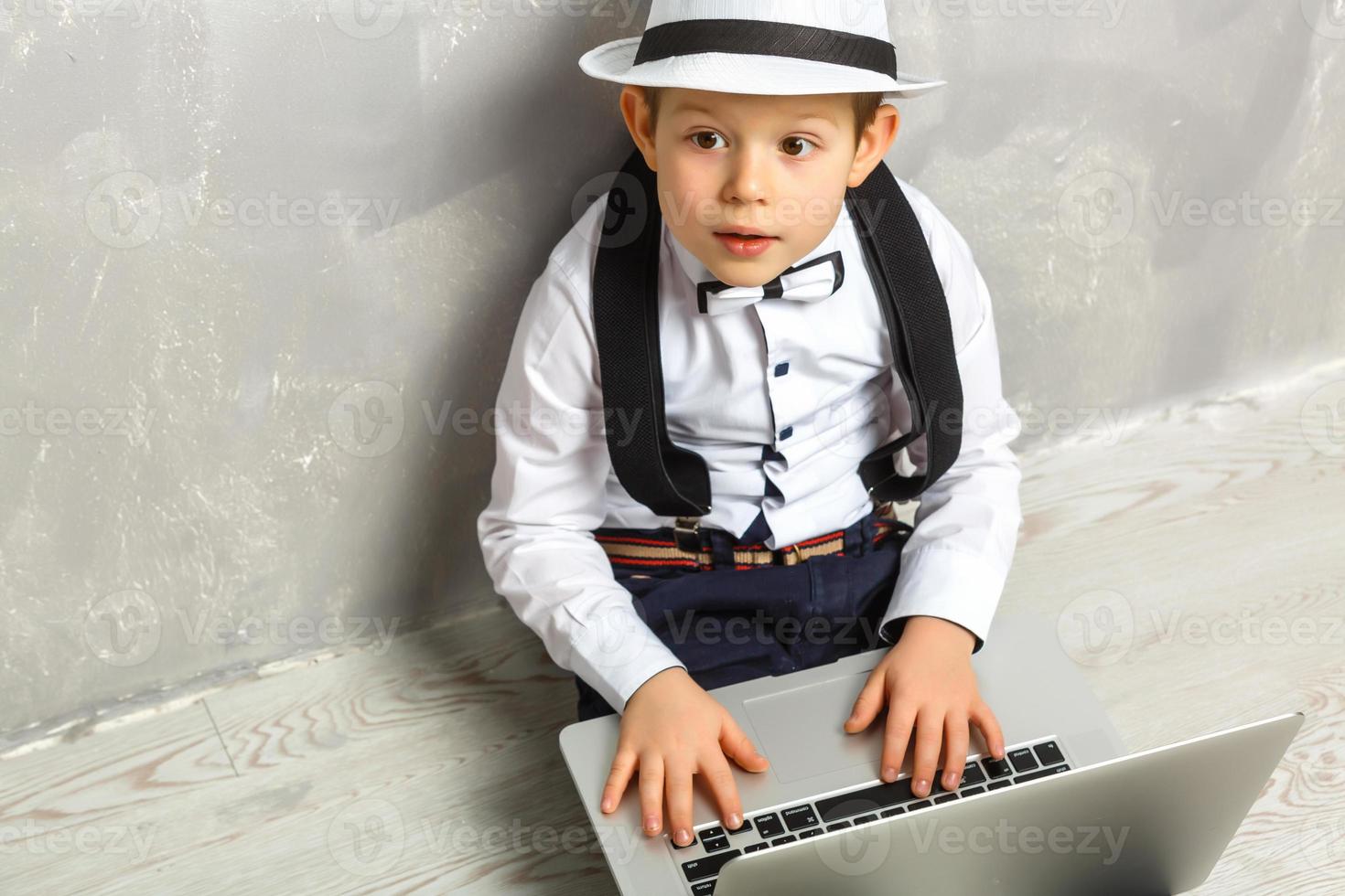 Portrait of Genius. Young boy working on the computer sitting On the floor. Studying. Online learning remotely. Distant school. Distance education. Online courses and knowledge. photo