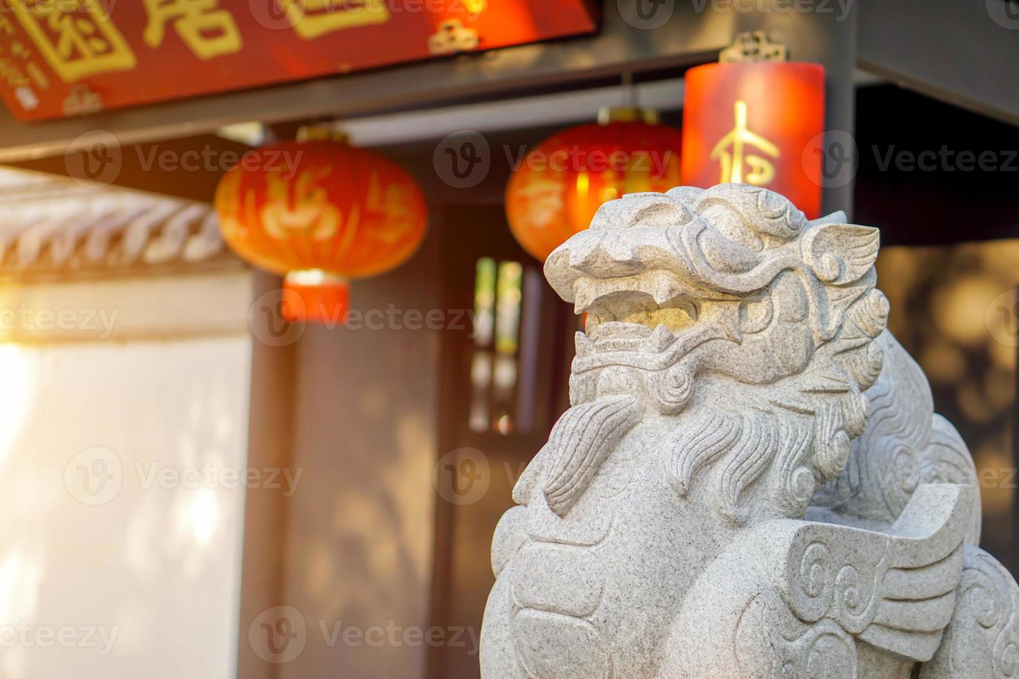 Closeup and crop Chinese lion figurine, stone sculpture in front of Chinese shrine on blurry Chinese shrine entrance with sun flare background. photo