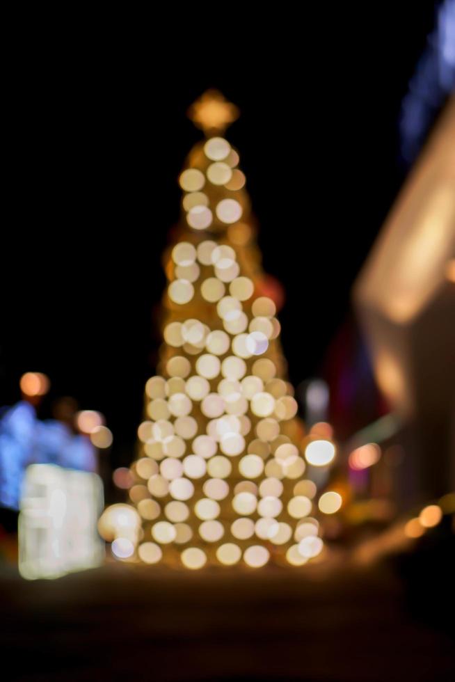 vista borrosa y bokeh del árbol de navidad y decorar la iluminación led frente al centro comercial en la noche de navidad en la ciudad urbana. foto