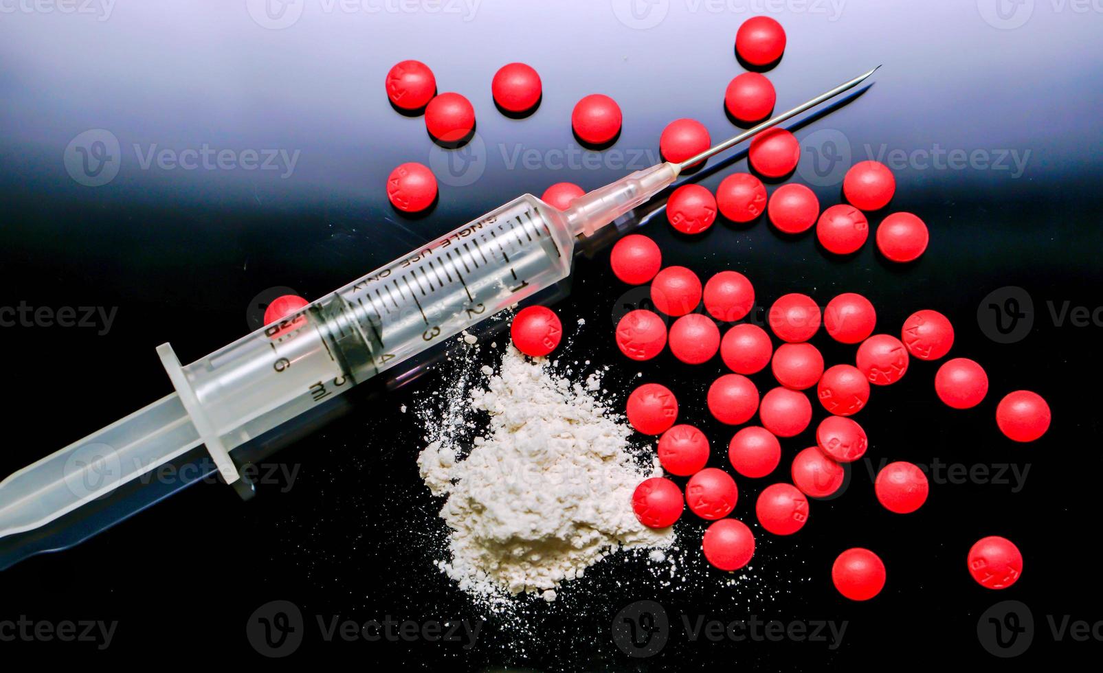 Plastic syringe put in a medical needle and white powder with red pill medicine isolate on black background. Suppose to heroin and amphetamine or narcotic addiction. photo