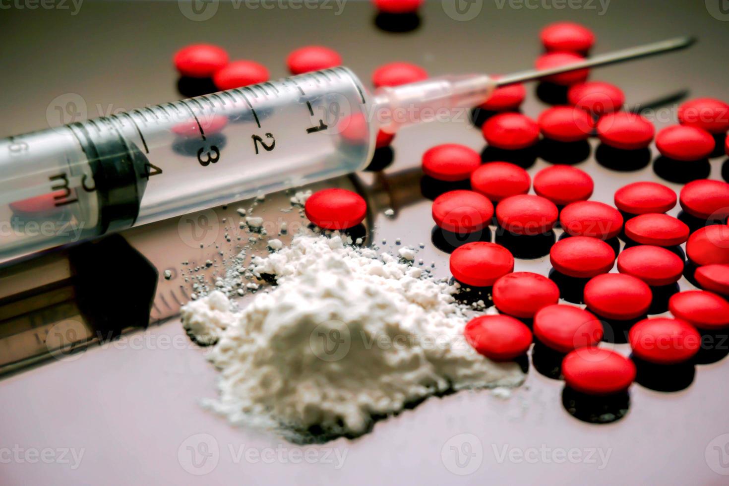 Plastic syringe put in a medical needle and white powder with red pill medicine isolate on black background. Suppose to heroin and amphetamine or narcotic addiction. photo