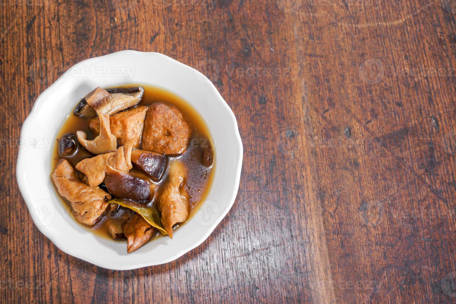 Top view Chinese vegetarian food Tofu and dry vegetables stewed in the gravy on white ceramic bowl and wooden table with copy space for texts background. photo