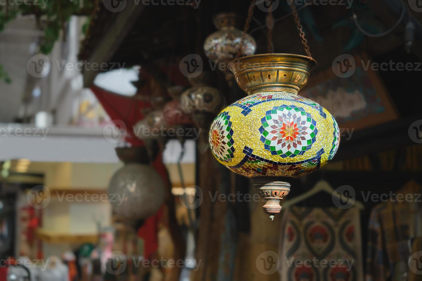 Market with handmade traditional colorful Turkish lamps and lanterns, selective focus on lantern, blurred background, popular souvenir lanterns hanging in shop for sale. photo