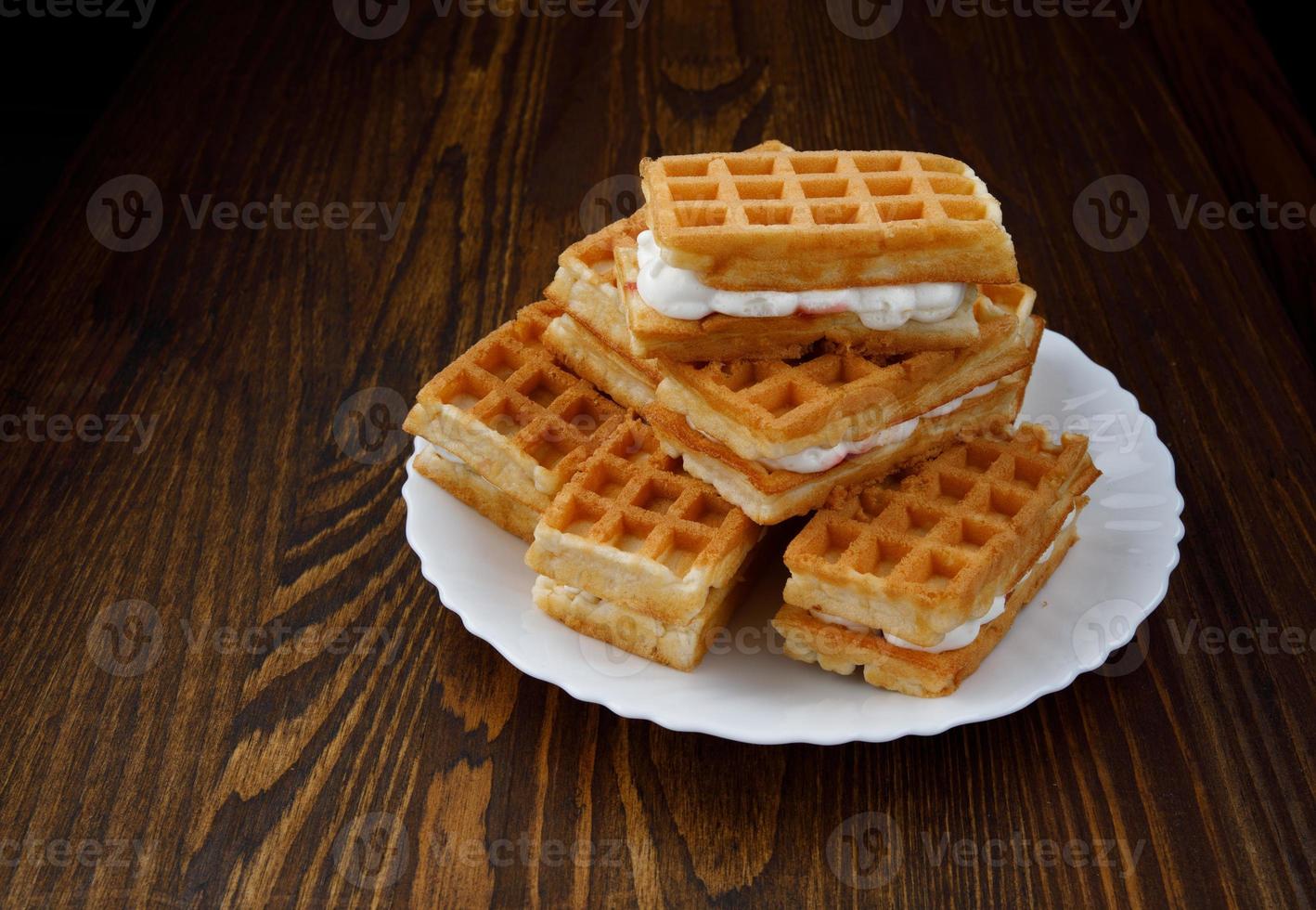 A pile of ruddy Viennese waffles lie on a white plate on a wooden background. photo