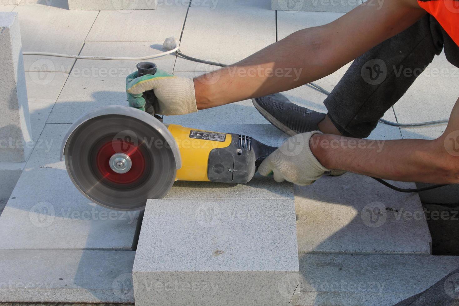 Hands of worker with electric grinder trims paving slabs on the construction site. Concept of laying new sidewalk tile. Stone cutting equipment. Road works. Civil engineering. Repair asphalt. Close-up photo