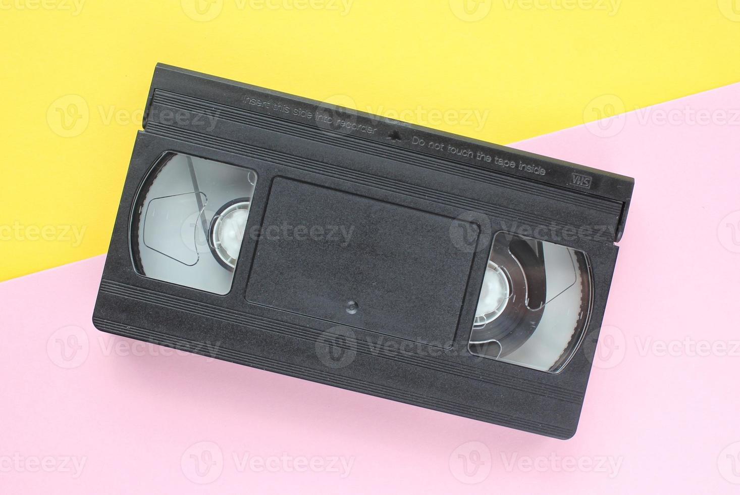 Black VHS videotape cassette on yellow and pink background. Old obsolete technology for tape recording and watching media movies. Retro, vintage, history, nostalgia concept. Top view, flat lay photo