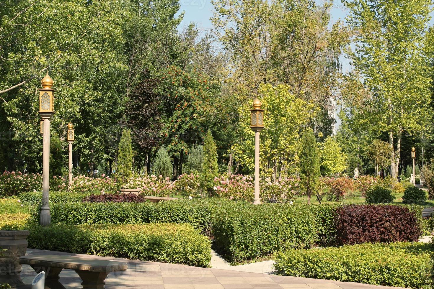 Trees and flowers in city park with Indian style lantern. Pedestrian zone for walking. Urban planning, public space concept. Town recreation area. Architecture design comfortable garden. Footpath way photo