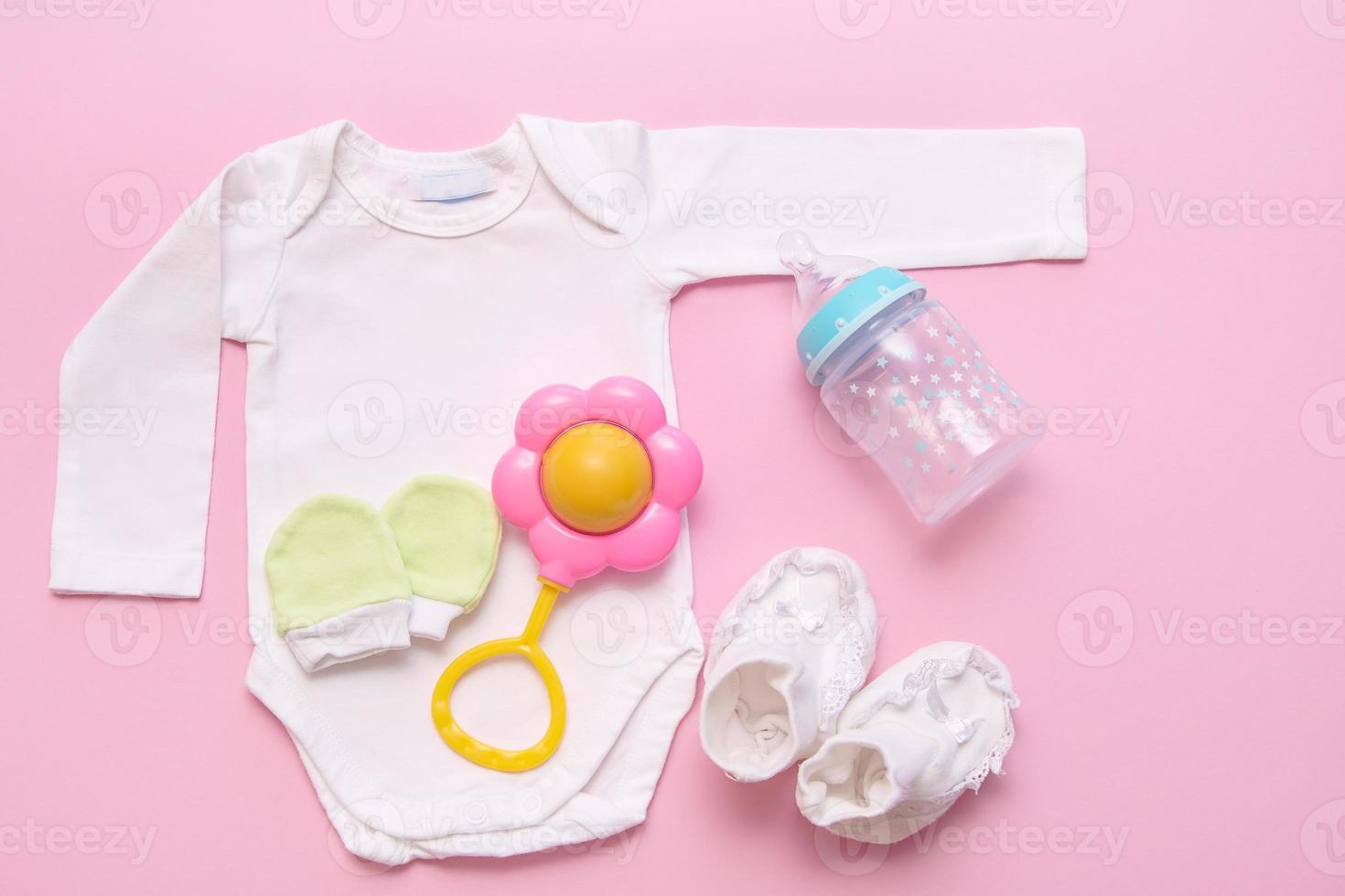 bodysuit, booties, mittens, rattle, bottle for mixture on a pink background, newborn photo