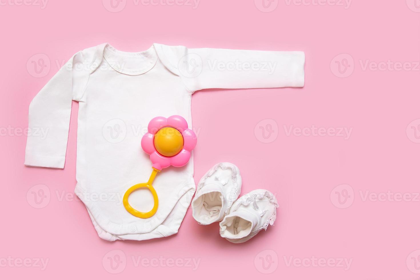 bodysuit, rattle and booties for a newborn on a pink background photo