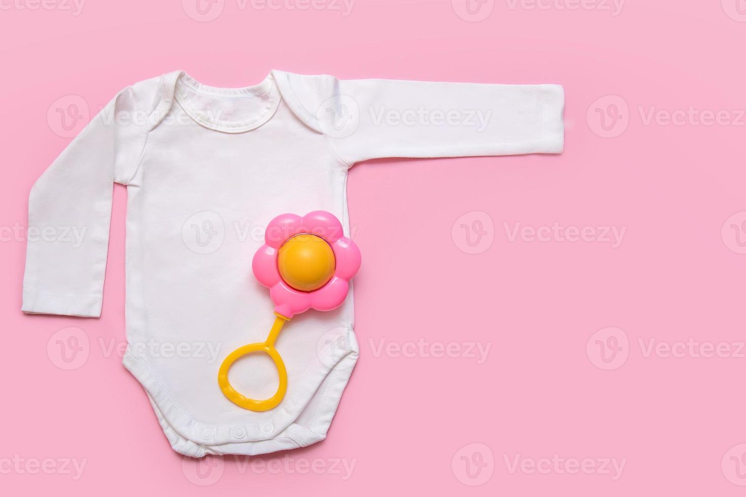 bodysuit for a newborn with a rattle on a pink background with copyspace photo