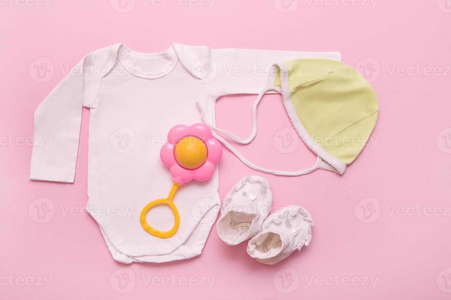 bodysuit, green cap, rattle and white booties for a newborn on a pink background photo