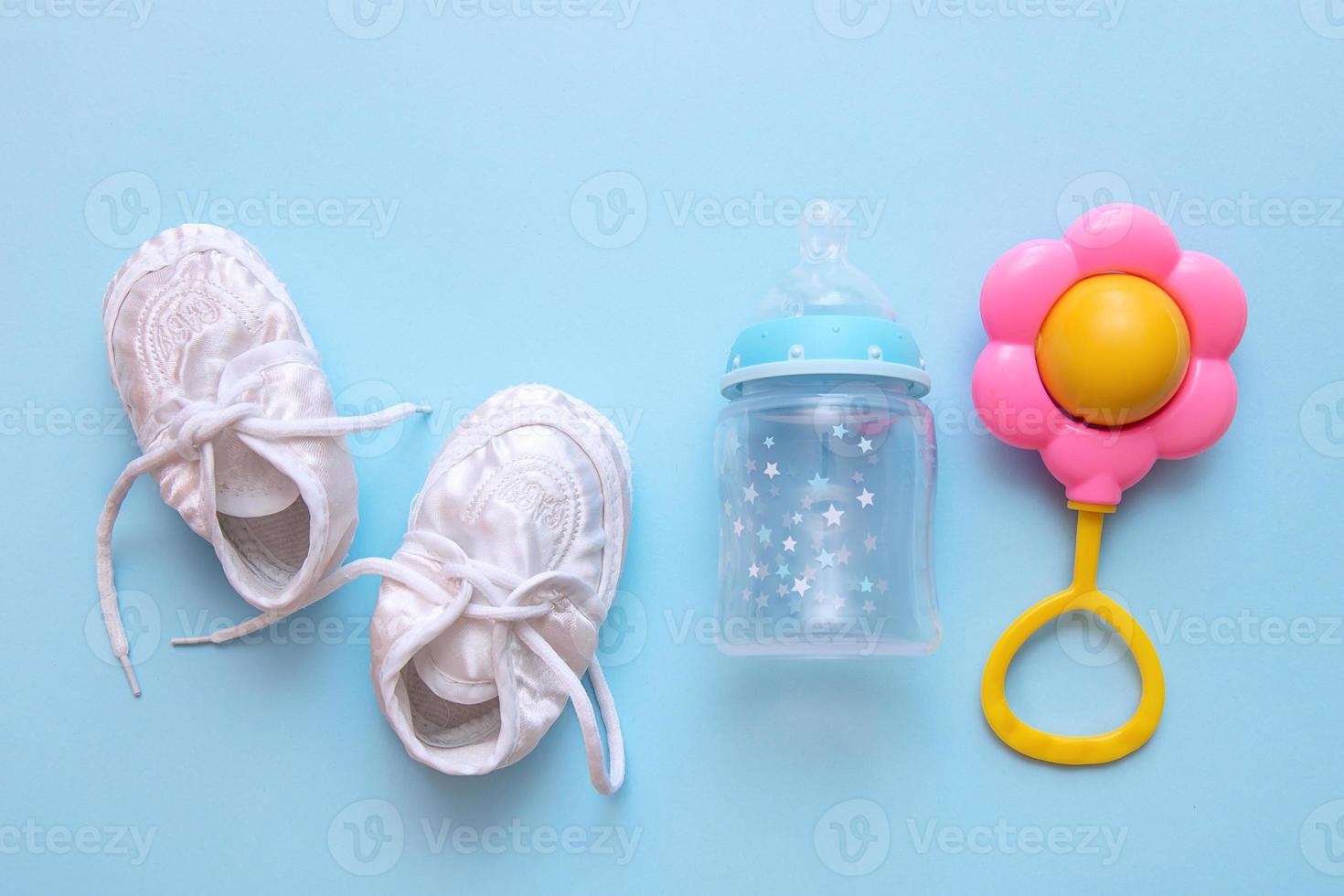 baby booties, formula bottle and rattle on blue background photo